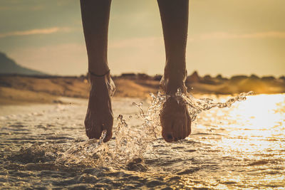Low section of person standing on land against sky during sunset