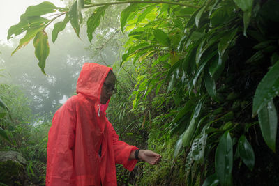 Woman wearing orange raincoat while standing in forest during rainy season