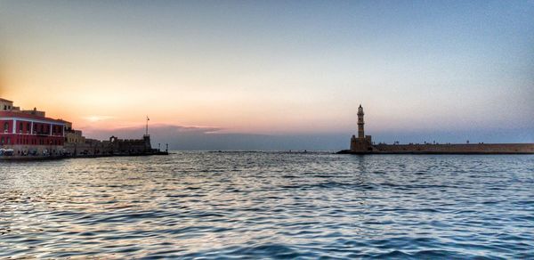 Buildings by sea against sky during sunset