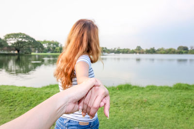 Woman wearing hat while standing on grass by lake against sky