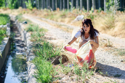 Young woman picking up garbage from dirt road