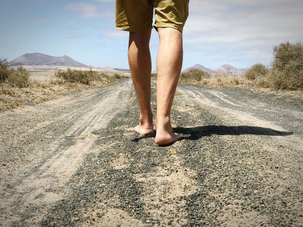 LOW SECTION OF MAN STANDING ON ROAD BY MOUNTAIN