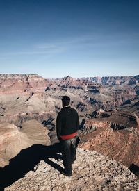 Rear view of man standing on rock against sky