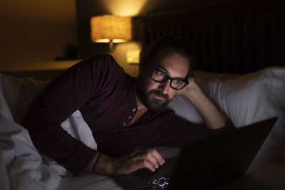 Trader using laptop lying on bed at night