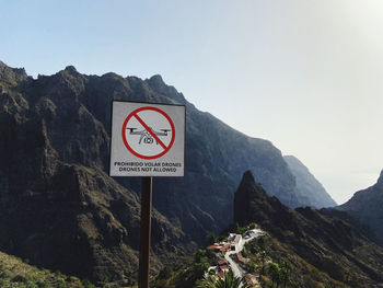 Road sign by mountain against clear sky