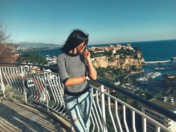 Woman sitting on railing against sea and cityscape