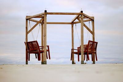 Empty swing construction out of benches against sky