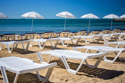 Deck chairs on beach by sea against sky