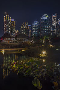 Illuminated buildings by river against sky at night