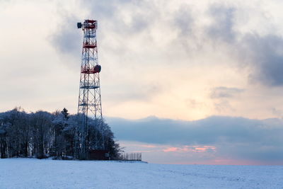Communications tower on snow covered land against sky during sunset