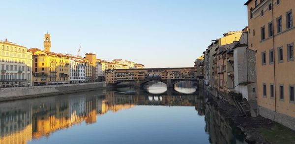 Arch bridge over river amidst buildings against clear sky
