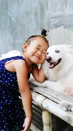 Cute girl playing with white dog against wall