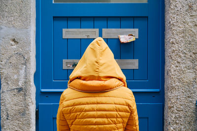 Rear view of person wearing raincoat standing in front of closed door