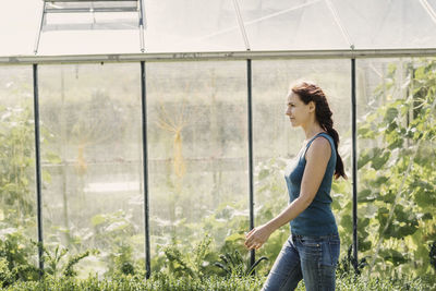 Female farmer walking against greenhouse on sunny day