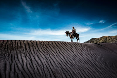 Mid adult man riding horse on sand at desert against sky