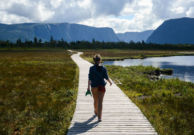 Rear view of woman walking on boardwalk by lake