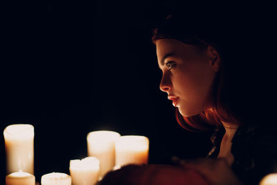 Young woman by candles in dark