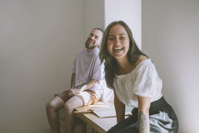 Cheerful hipster man with girlfriend sitting on table at home