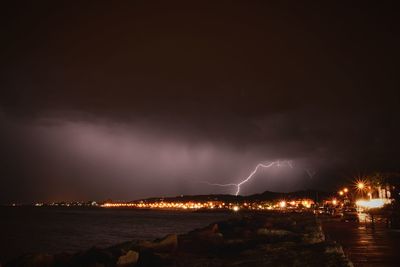 Illuminated city by sea against sky at night