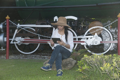 Woman using digital tablet while sitting against train