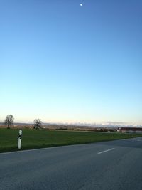 Road by landscape against clear blue sky