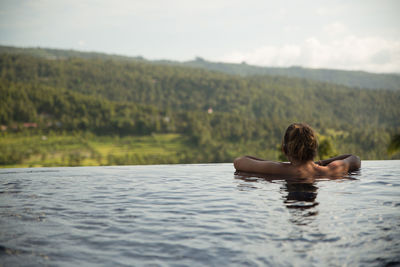 Rear view of young woman in infinity pool against clear sky