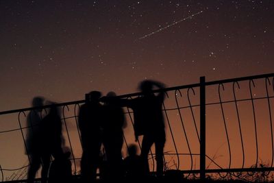 Men on railing by sea against sky at night