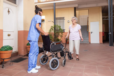 Happy senior woman with walking stick in wheelchair with her caregiver at home.