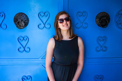 Young woman wearing sunglasses against blue wall