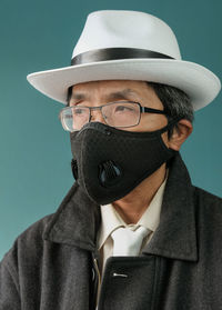 Man wearing mask and hat looking away against colored background