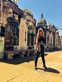 Full length of mature woman standing on footpath against old buildings during sunny day