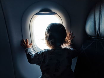 Rear view of baby girl looking through window in airplane