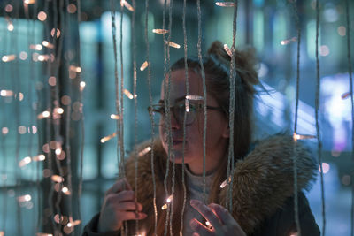 Young woman by illuminated string lights 