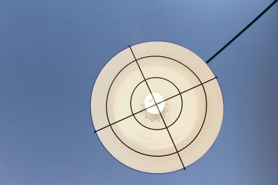 Low angle view of circular electric lamp against clear blue sky