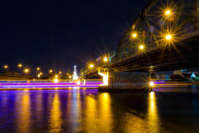 Illuminated bridge over river against sky at night