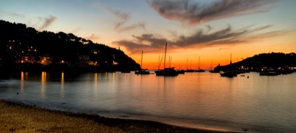 Silhouette sailboats in sea against sky during sunset
