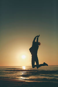 Woman jumping on beach at sunset