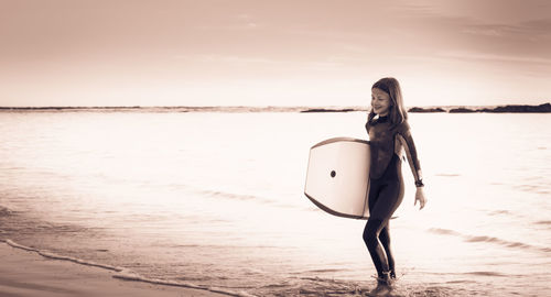 Girl carrying surfboard at beach during sunset