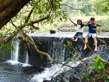 Kids sitting by waterfall in forest