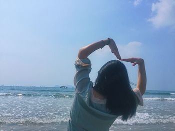 Woman with arms raised on beach against sky