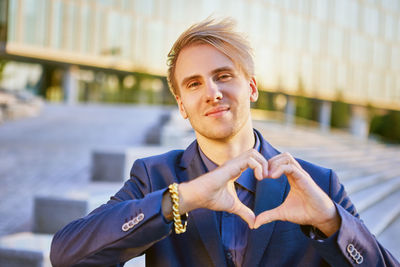 Portrait of smiling businessman making heart shape while standing outdoors