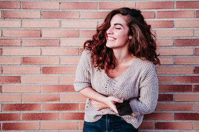 Beautiful young woman standing against brick wall