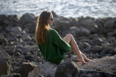 Beautiful woman sitting on rock at beach