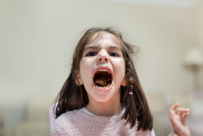 Portrait of cute girl with mouth open showing chocolate while sitting at home