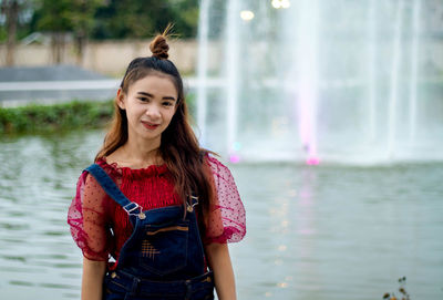 Portrait of smiling young woman standing against fountain