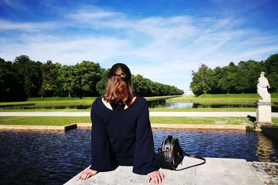 Rear view of woman sitting at lake against sky