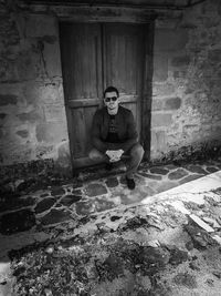 Portrait of young man sitting against wall