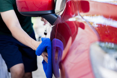 Midsection of man cleaning red car