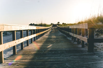 Wooden footbridge leading to water against clear sky