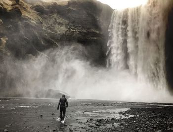 Rear view of man walking against skogafoss